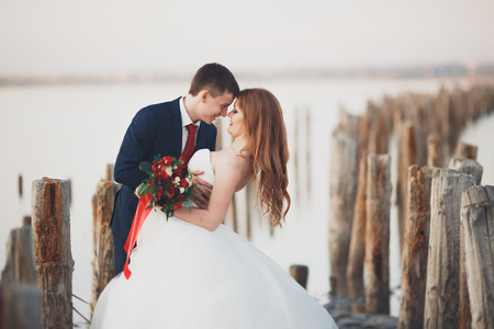 Wedding couple, groom, bride with bouquet posing near sea on sunset.の写真素材