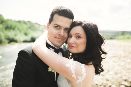 Close up portrait of couple against river and green trees. Beautiful young woman kissing handsome man outdoors.の写真素材