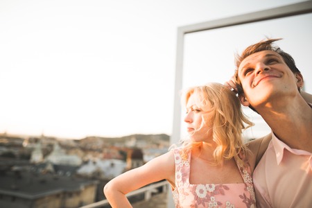 Pretty sunny outdoor portrait of young stylish couple while kissing on the roof with city view.