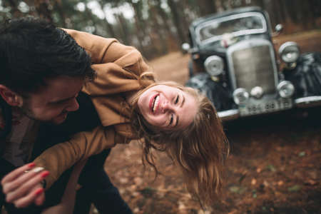 Gorgeous newlywed bride and groom posing in pine forest near retro carの写真素材