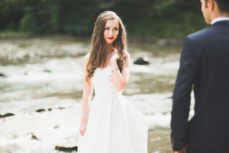 Beautifull wedding couple kissing and embracing near the shore of a mountain river with stonesの写真素材