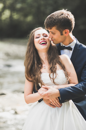 Beautifull wedding couple kissing and embracing near the shore of a mountain river with stonesの写真素材