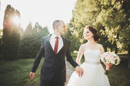 Stylish couple of happy newlyweds walking in the park on their wedding day with bouquetの写真素材