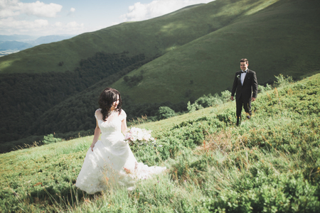 Young newly wed couple, bride and groom kissing, hugging on perfect view of mountains, blue sky.の写真素材