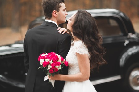 Stylish wedding couple, bride, groom kissing and hugging near retro car in autumnの写真素材
