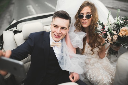 Happy bride and groom making selfie at their wedding in retro carの写真素材