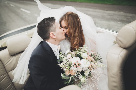 Stylish wedding couple, bride, groom kissing and hugging on retro carの写真素材