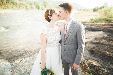 Elegant gentle stylish groom and bride near river with stones. Wedding couple in loveの写真素材
