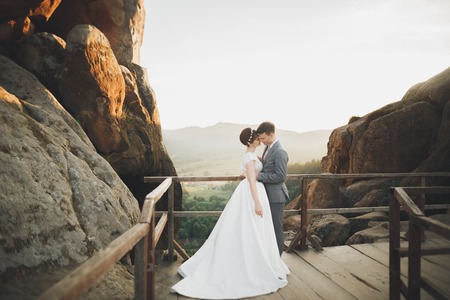 Gorgeous bride and stylish groom walking at sunny landscape, wedding couple, luxury ceremony mountains with amazing view, space for textの写真素材