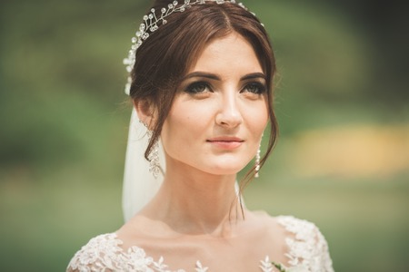 Beautiful bride in elegant white dress holding bouquet posing in parkの写真素材