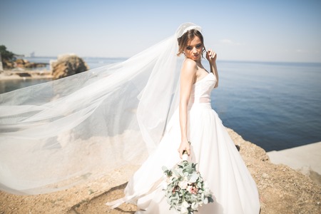 Lovely bride in white wedding dress posing near the sea with beautiful backgroundの写真素材