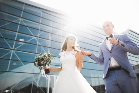 Lovely happy wedding couple, bride with long white dress posing near modern buildingの写真素材