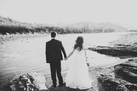 Happy newlywed couple posing and smiling in wedding dress and suit outdoor, black and white