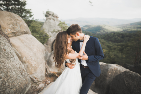 Gorgeous bride, groom kissing and hugging near the cliffs with stunning viewsの写真素材