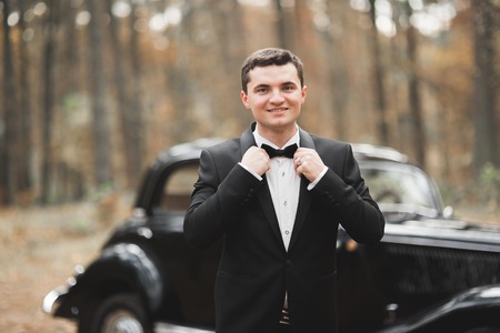 Handsome groom at wedding smiling and waiting for bride near retro carの写真素材