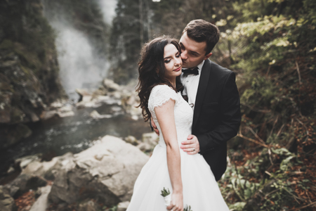 Beautifull wedding couple kissing and embracing near the shore of a mountain river with stonesの写真素材