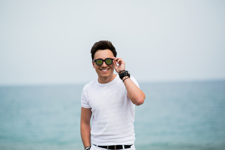 Portrait of young man in sunglasses smiling on the beachの写真素材
