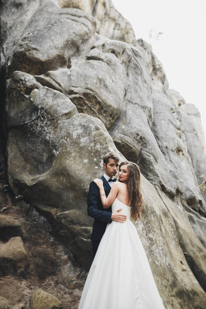 Gorgeous bride, groom kissing and hugging near the cliffs with stunning viewsの写真素材