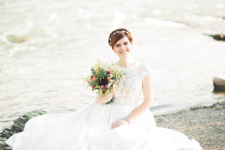Gorgeous beautiful bride smiles while posing by the river with bouquetの写真素材
