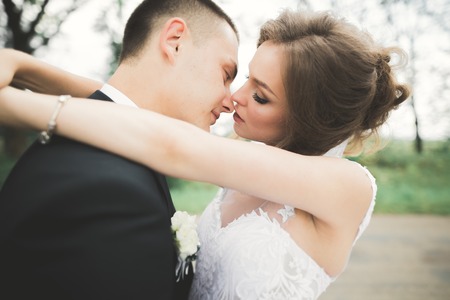 Stylish couple of happy newlyweds walking in the park on their wedding day with bouquetの写真素材