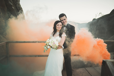 Wedding couple posing near rocks with colored smoke behind themの写真素材