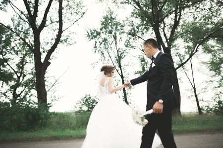 Stylish couple of happy newlyweds walking in the park on their wedding day with bouquetの写真素材