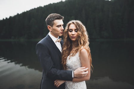 Young newly wed couple, bride and groom kissing, hugging on perfect view of mountains, blue skyの写真素材