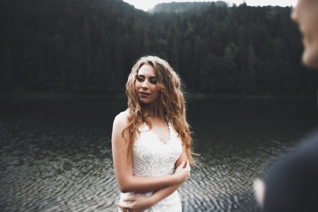 Young newly wed couple, bride and groom kissing, hugging on perfect view of mountains, blue skyの写真素材
