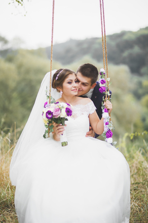 Romantic, fairytale, happy newlywed couple hugging and kissing in a park, trees in backgroundの写真素材