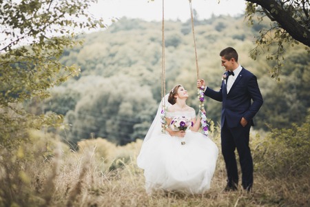 Romantic, fairytale, happy newlywed couple hugging and kissing in a park, trees in backgroundの写真素材
