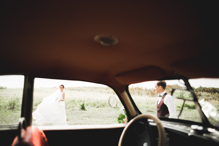 Stylish wedding couple, bride, groom kissing and hugging on retro carの写真素材