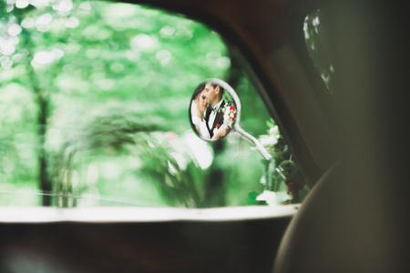 Stylish wedding couple, bride, groom kissing and hugging on retro carの写真素材