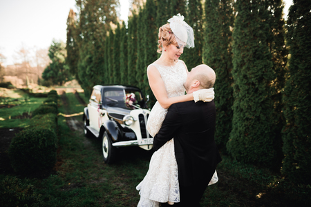 Happy newlywed couple, man and wife kissing near stylish retro carの写真素材