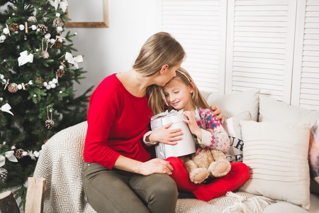 Merry Christmas and Happy Holidays. Cheerful mom and her cute daughter girl exchanging giftsの写真素材