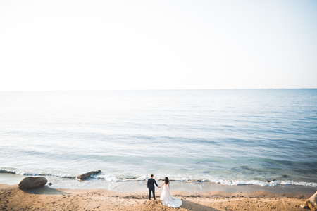 Wedding couple, groom, bride with bouquet posing near sea and blue skyの写真素材