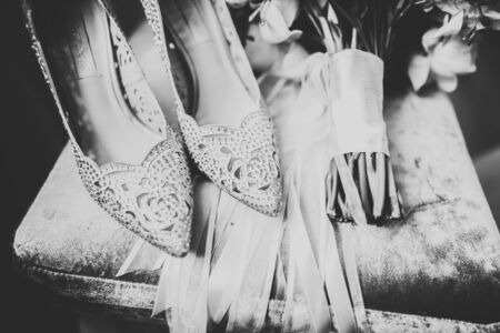 Brides wedding shoes with a bouquet with roses and other flowers on tha arm chair.の写真素材