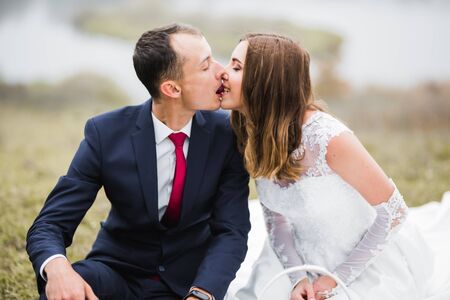 Beautiful bride and groom embracing and kissing on their wedding day outdoorsの写真素材