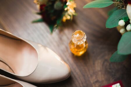 Pair of elegant and stylish bridal shoes with wedding rings and a bouquet of roses and other flowersの写真素材