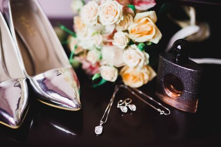 Brides wedding shoes and costume jewellery with a bouquet with roses and other flowers.の写真素材