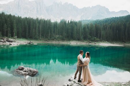 Young couple near lake Karersee, Italy. Holding hands at the stone at lake.