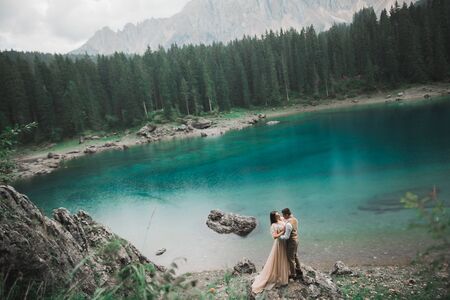 Gorgeous happy couple standing close to each other and looking in eyes near a beautiful lake in the mountains.の写真素材