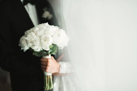 Beautiful young wedding couple posing with bouquet of flowers in hands.