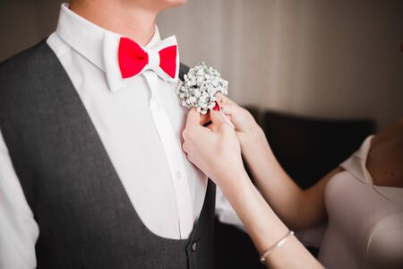 Bride pins white boutonniere with green leaves to groom's jacket.