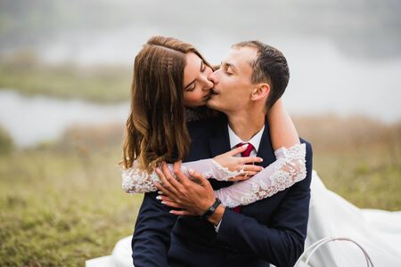 Beautiful bride and groom embracing and kissing on their wedding day outdoorsの写真素材