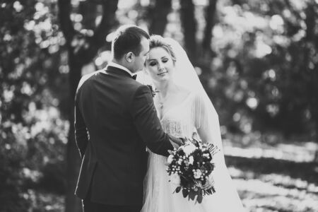 Romantic, fairytale, happy newlywed couple hugging and kissing in a park, trees in backgroundの写真素材