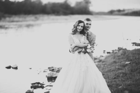 Wedding couple, groom and bride hugging, outdoor near riverの写真素材