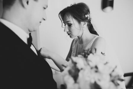 Beautiful bride putting on boutonniere with roses on groom suitの写真素材