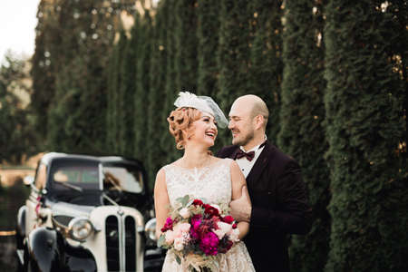 Happy newlywed couple, man and wife kissing near stylish retro carの写真素材