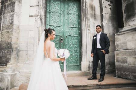 Wedding photo shooting. Bride and bridegroom walking in the city. Married couple embracing and looking at each other. Holding bouquetの写真素材