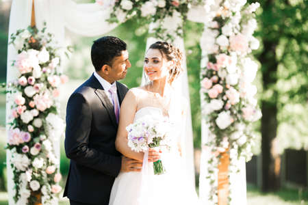 Beautiful young wedding couple posing with bouquet of flowers in handsの写真素材